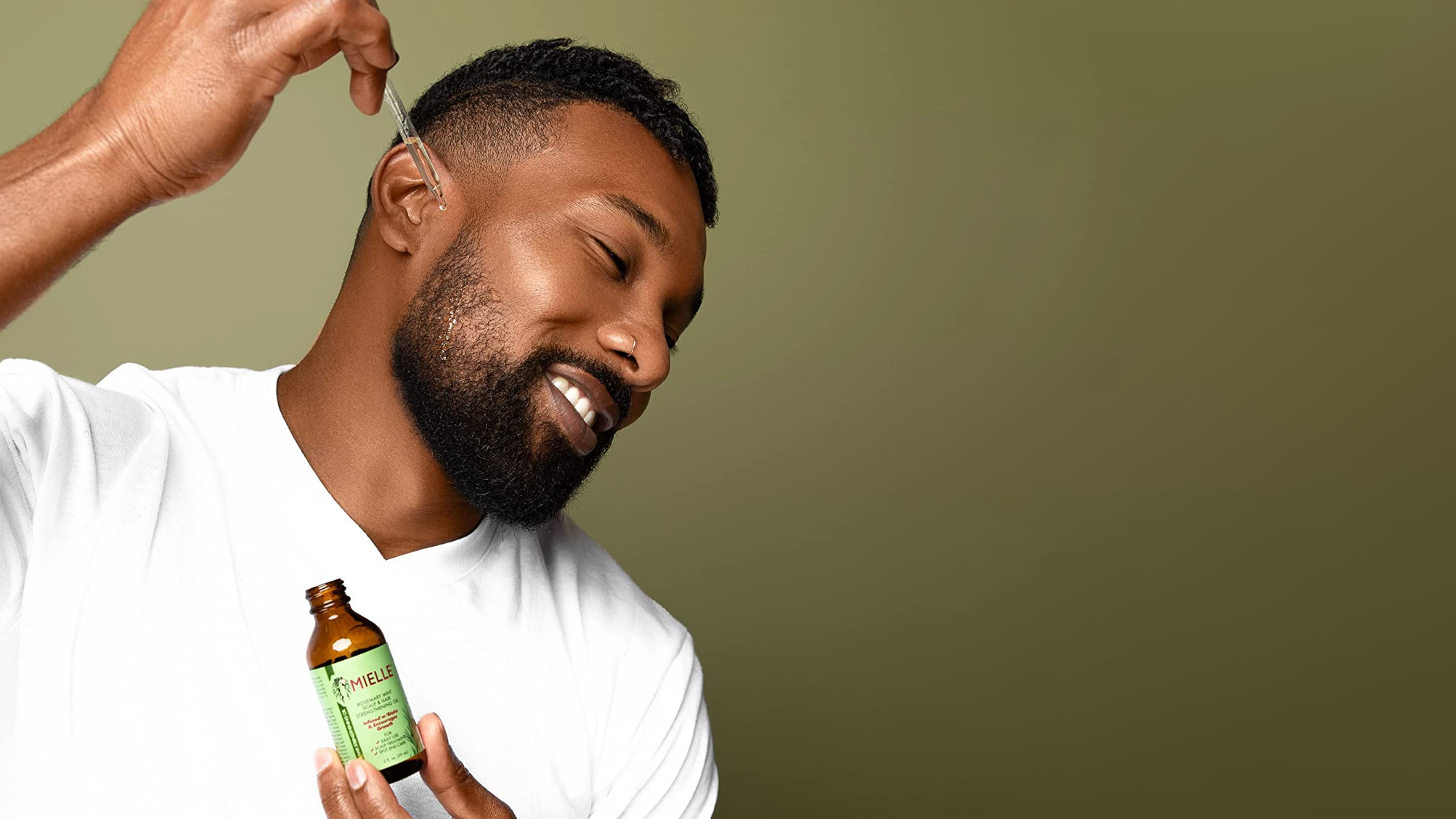 A black man using Mielle Organics rosemary mint oil on his beard.
