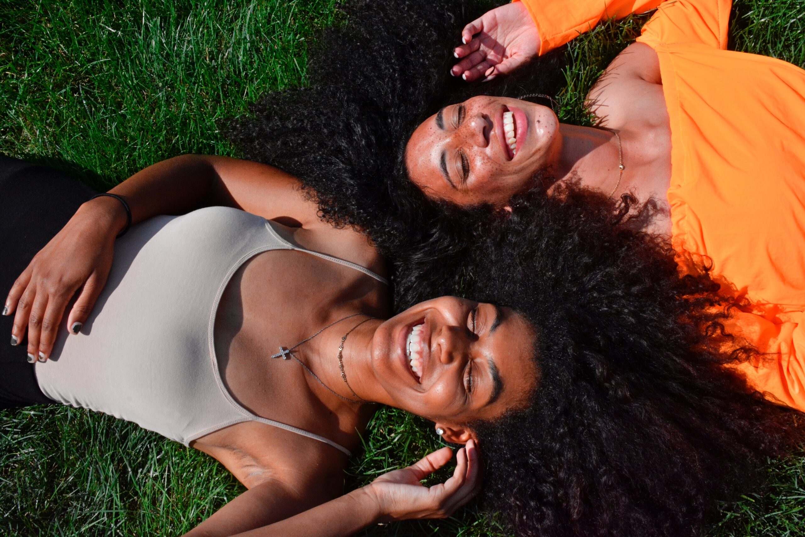 Sherry's cosmetics - two black women with beautiful afro hair laying on the grass laughing