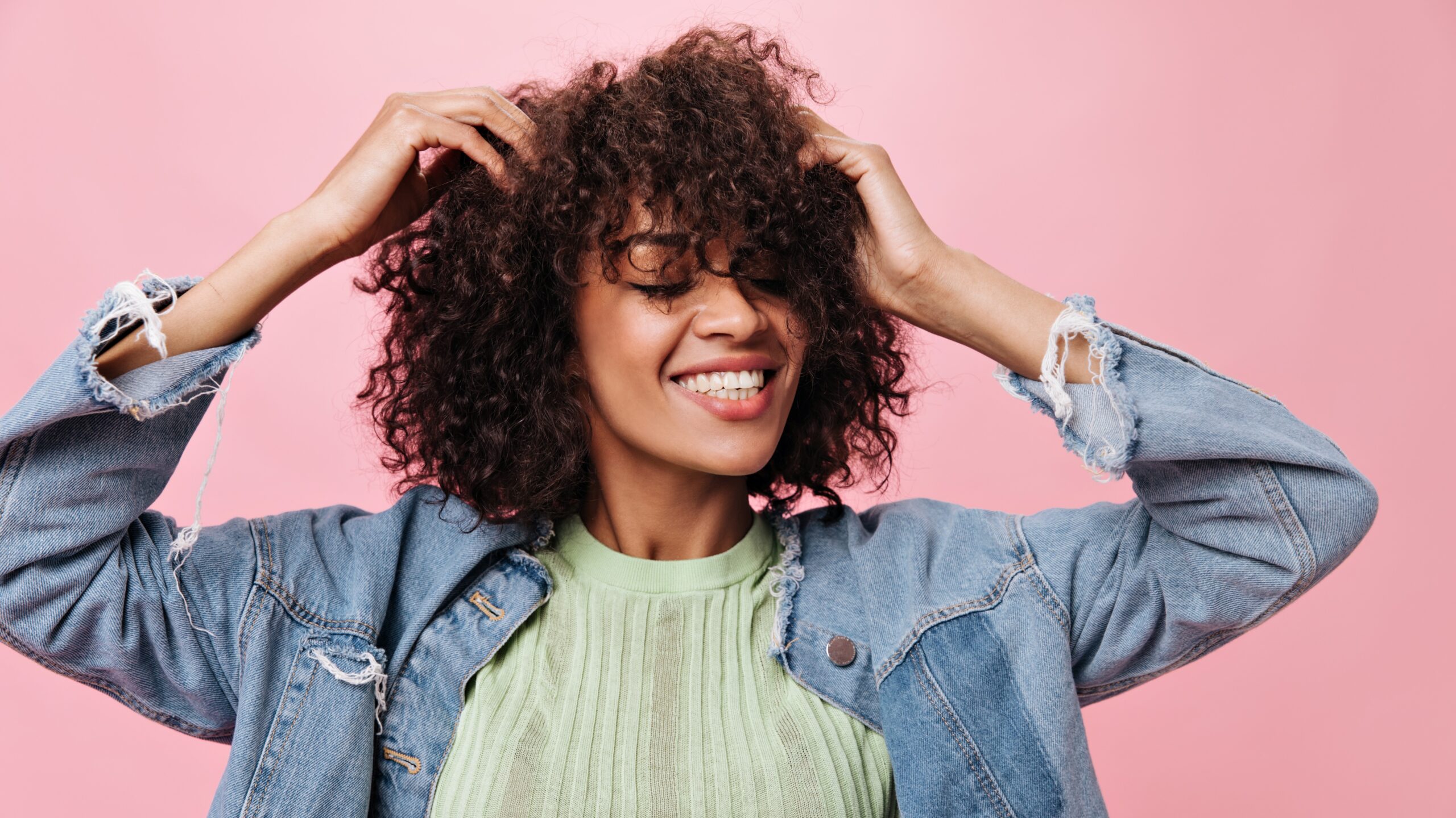 Young girl dances happy on pink background and touches her curly hair